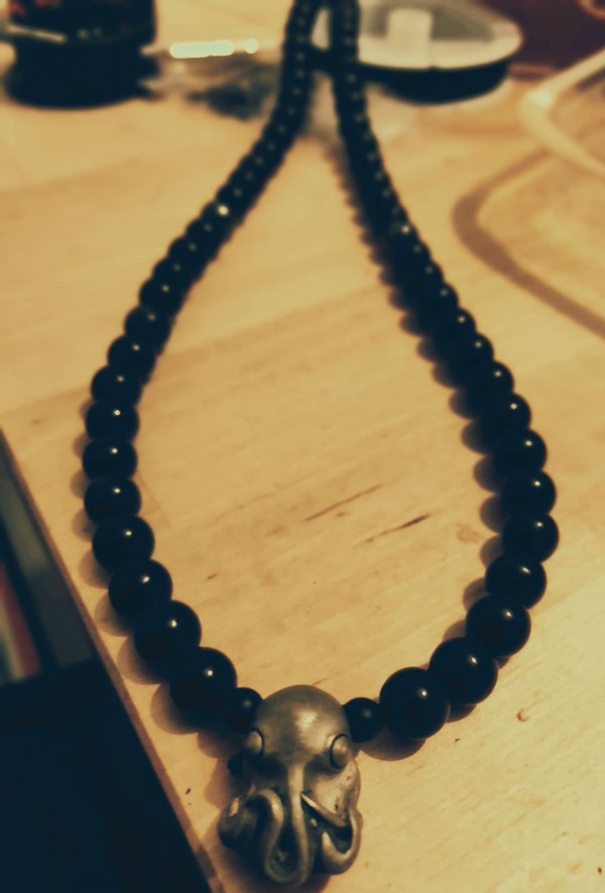 Collier fait main avec pendentif poulpe en argent et perles sombres, posé sur un établi en bois.