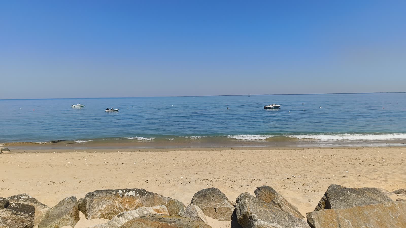 Vue lumineuse sur la plage et la mer calme de Noirmoutier, avec plusieurs petits bateaux au mouillage.
