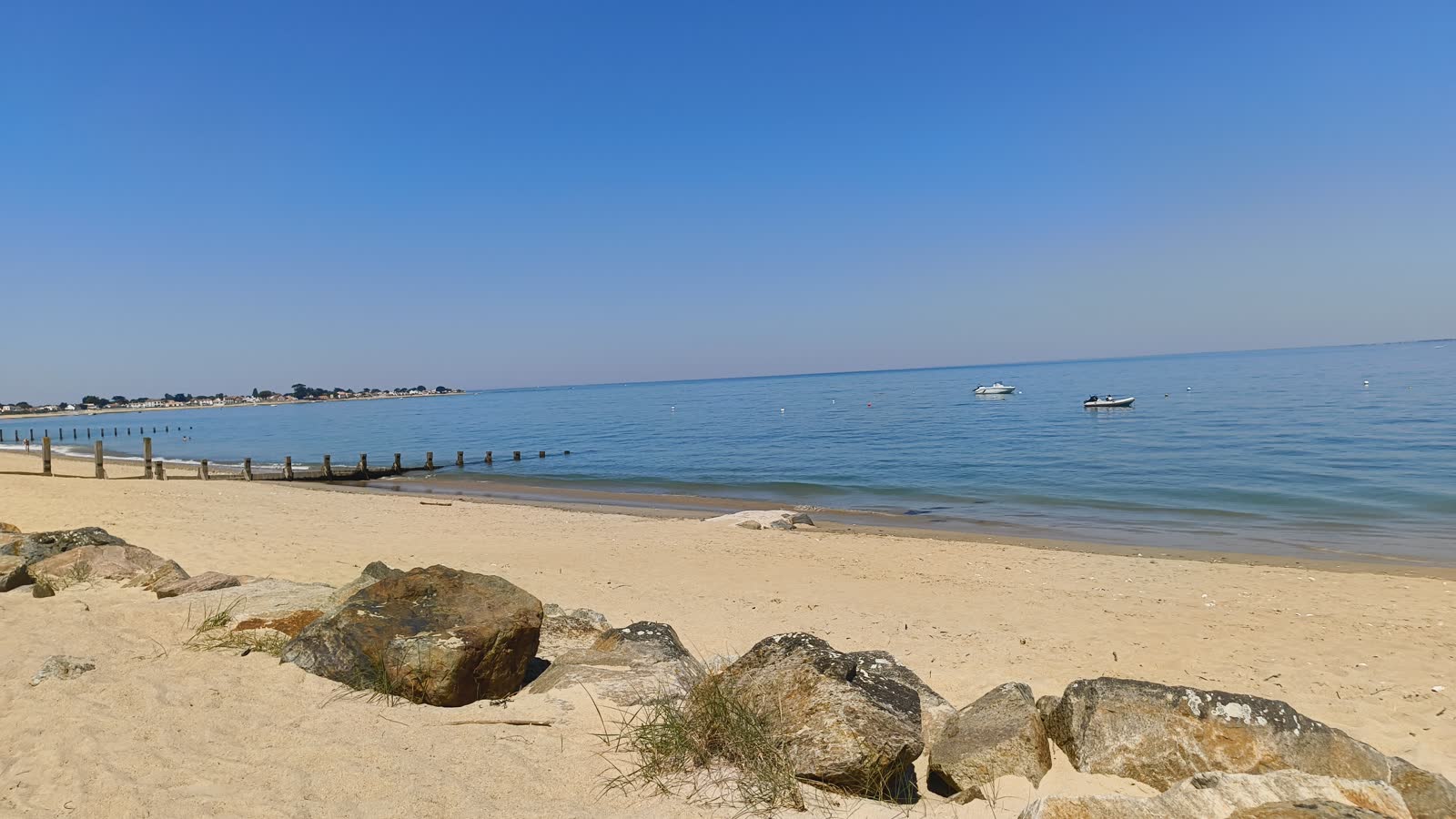 Plage de Noirmoutier avec rochers au premier plan, mer calme et petits bateaux au mouillage.